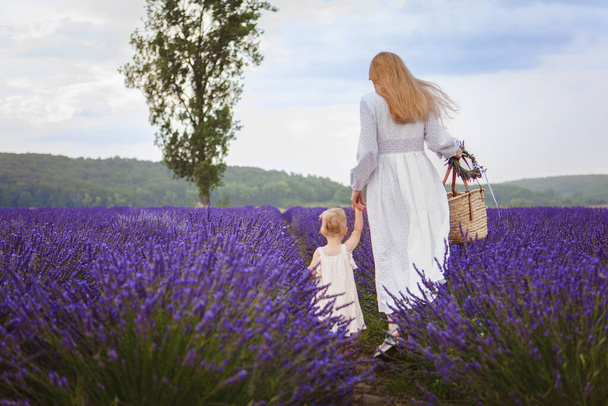 Beim Spaziergang durch Lavendelfelder mit ihrer kleinen Tochter sieht man die Mutter, wie sie sich um ihre Tochter kümmert - Foto, Bild