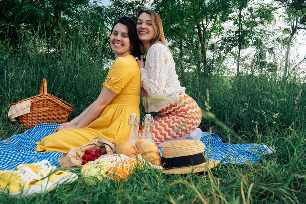 Δύο κορίτσια σε ραντεβού κάθονται σε μια μπλε κουβέρτα για πικνίκ στη φύση - Φωτογραφία, εικόνα