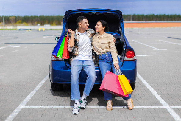 Szczęśliwa afrykańska para pozowanie z kolorowymi torbami shopper w pobliżu samochodu na zewnątrz, odpoczynek po udanym zakupy w centrum handlowym w weekend, wolne miejsce - Zdjęcie, obraz
