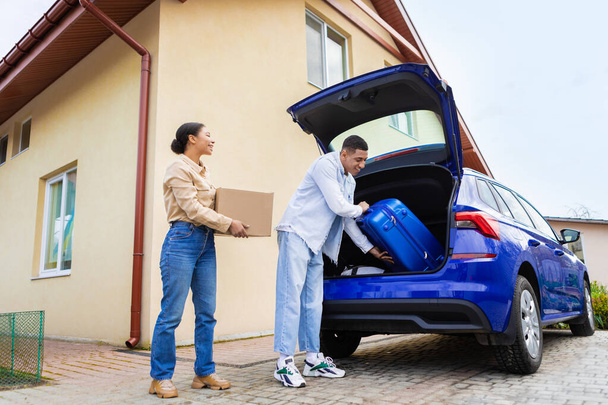 Boldog afro-amerikai pár megy nyaralni, megpakolják az autó csizmáját utazási bőröndökkel, férj és feleség kinyitják az autó hátulját, csomagokat szállítanak. - Fotó, kép
