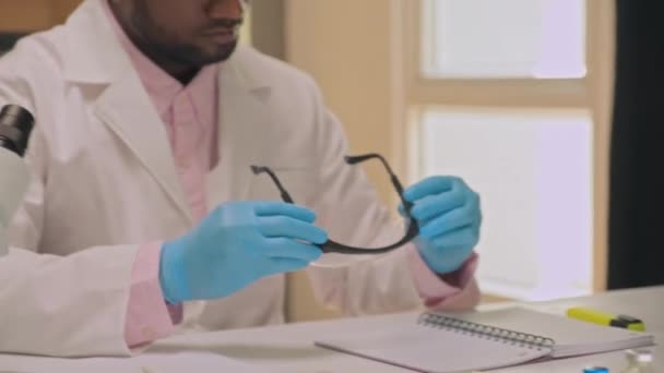 Наклоните снимок ученого надевающего защитные очки в униформе в лаборатории - Кадры, видео