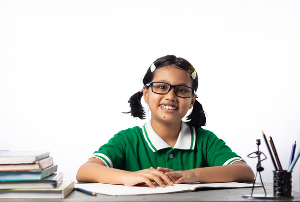 Una bella studentessa indiana con gli occhiali che studia sul tavolo di studio su sfondo bianco - Foto, immagini