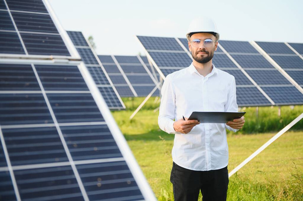Positive bearded male investor standing against photovoltaic panels producing alternative energy - Φωτογραφία, εικόνα