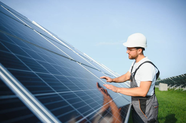 Side view of male worker installing solar modules and support structures of photovoltaic solar array. Electrician wearing safety helmet while working with solar panel. Concept of sun energy. - Valokuva, kuva