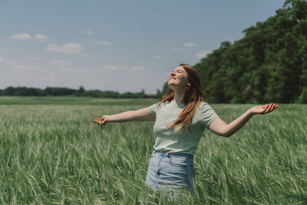 A woman enjoys the fresh air in nature in a green barley field. Summer countryside and gathering flowers. Atmospheric tranquil moment - Foto, Imagem
