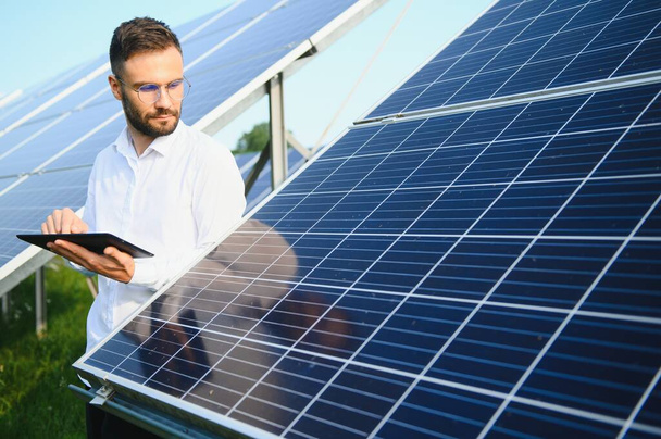 Male worker solar power plant with a tablet on a background of photovoltaic panels - Foto, afbeelding