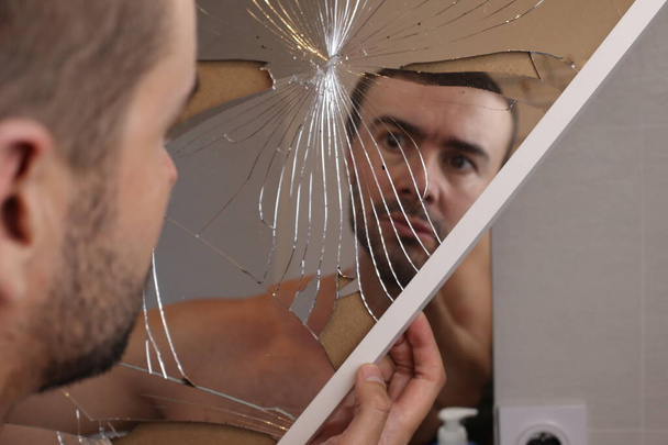 retrato de un joven frente a un espejo roto en el baño - Foto, Imagen