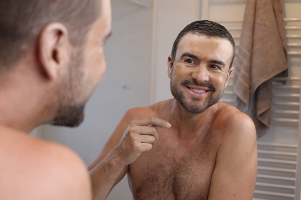 портрет молодого человека с витилиго перед зеркалом в ванной комнате - Фото, изображение