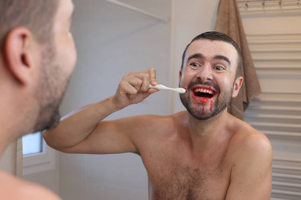 портрет молодого чоловіка з яснами, що чистить зуби перед дзеркалом у ванній
 - Фото, зображення