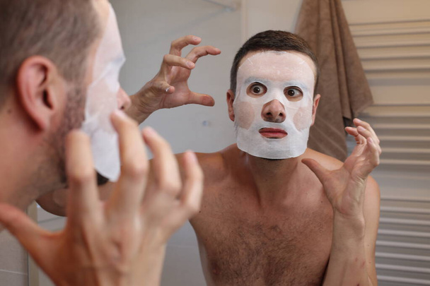 portré fiatal férfi bőr maszk előtt tükör a fürdőszobában - Fotó, kép