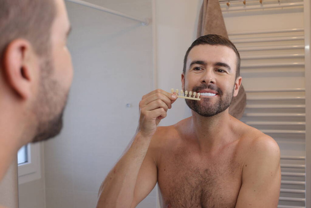 浴室の鏡の前にプラスチック製の歯のサンプルを持つ若い男の肖像画 - 写真・画像