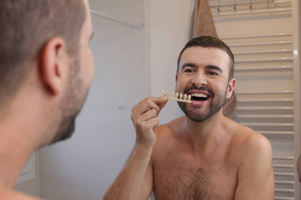 portrait de jeune homme avec des échantillons de ton de dents en plastique devant le miroir dans la salle de bain - Photo, image