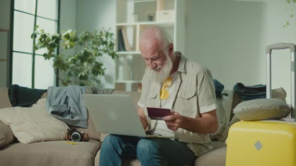 Een gelukkige oude man voert gegevens van zijn paspoort in op een laptop. Een glimlachende oudere man bereidt zich voor op een reis, verheugt zich op succes op het internet. Online boeken. Winteravonturen. - Video