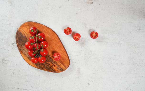 Vibrant small red tomatoes with green vines on wooden chopping board, white stone table under, view from above. - Foto, afbeelding