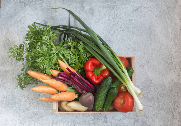 verse groenten in een houten doos. wortels, aardappelen, bieten, komkommers, tomaten, groene uien, paprika 's - Foto, afbeelding