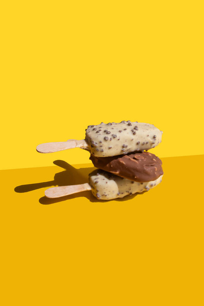 white and milk chocolate, ice cream stick balance on a yellow background - Foto, Imagen