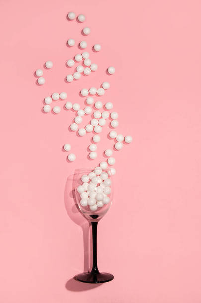 Wine glass with white shiny beads on a pink background. Creative minimal party concept. - Foto, Imagem