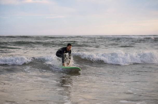 Aktywność sportowa. Młody przystojniak surfujący na plaży, wysportowany młody surfer w kombinezonie wodnym Fale na desce surfingowej, Millennial Mężczyzna cieszący się aktywnym stylem życia, Kopiuj przestrzeń - Zdjęcie, obraz