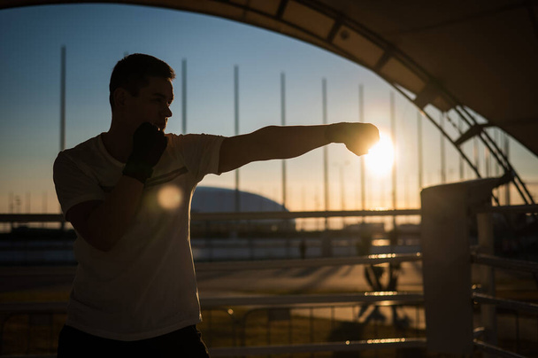 A man trains in boxing at the stadium at sunset. Athlete silhouette - Fotoğraf, Görsel