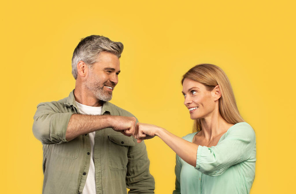 Csapatmunka. Boldog középkorú férfi és nő ütő ököl és mosolygós, ünneplő siker partnerség diadal álló sárga stúdió háttér - Fotó, kép