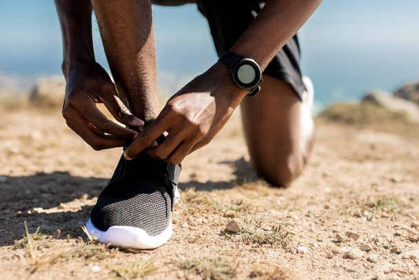Training, healthy lifestyle concept. Closeup view of unrecognizable black man tying his shoelaces before jogging outdoors in the morning, wearing sneakers - Photo, Image