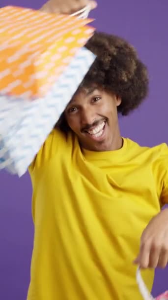 Glücklicher afrikanischer Mann lächelt in die Kamera, während er im Studio Einkaufstüten zeigt - Filmmaterial, Video