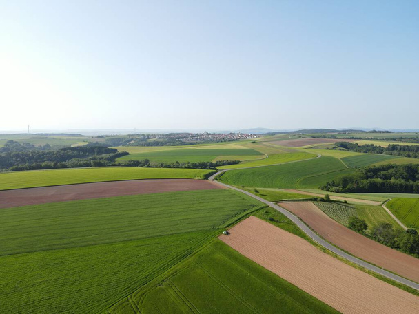 Вид з повітря на ландшафт з зеленими сільськогосподарськими полями, асфальтована дорога і блакитне сонячне небо на початку літа  - Фото, зображення