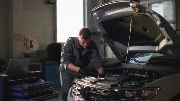 giovane meccanico professionista che ripara il motore dell'automobile con un cappuccio aperto usando la chiave inglese alla stazione di servizio - Filmati, video