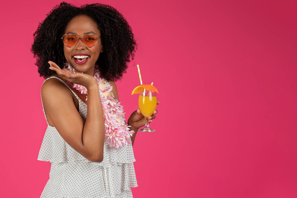 Cheerful young black curly lady in sunglasses enjoys tropical cocktail, isolated on pink background, studio. Trip, fun at summer vacation, party and relax emotions, lifestyle, ad and offer - Fotografie, Obrázek