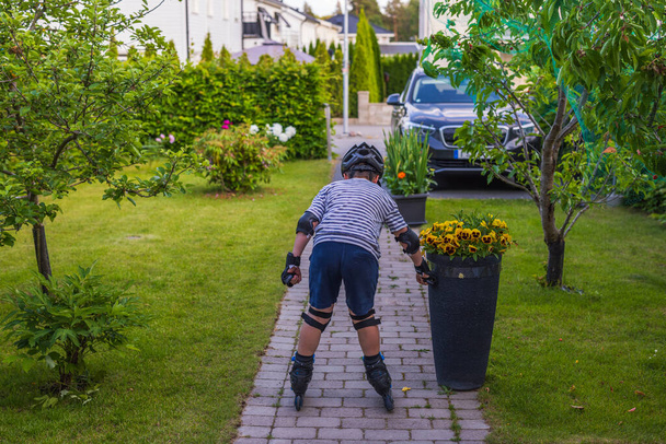 Close up view of young boy learning inline skating in garden on sunny summer day. Sweden. - Photo, Image