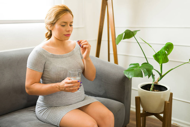 Mulher muito grávida na casa dos 30 anos tomando vitaminas e suplementos para a gravidez em casa - Foto, Imagem