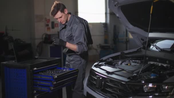 giovane professionista dipendente servizio auto maschile utilizzando una chiave inglese riparazione di un motore di auto presso la stazione di servizio - Filmati, video
