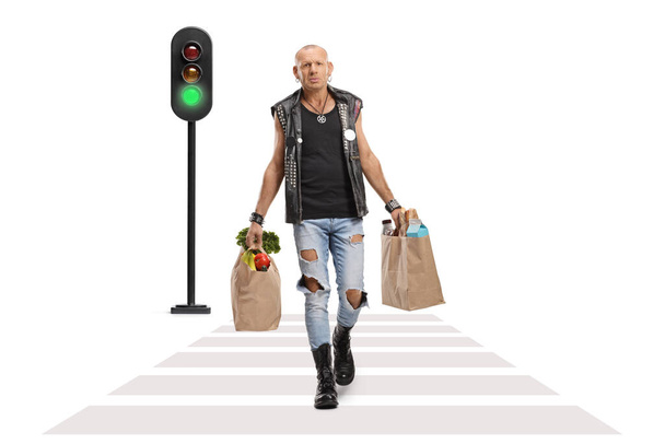 Full length portrait of a punk carrying grocery bags and walking across a street isolated on white background - Fotó, kép