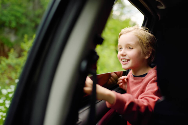 Cute preteen boy looking out through window of car during family road trip and enjoy of pleasant expectation of happy vacation. Joyful child travel with parents while holidays. Go everywhere. - Photo, Image