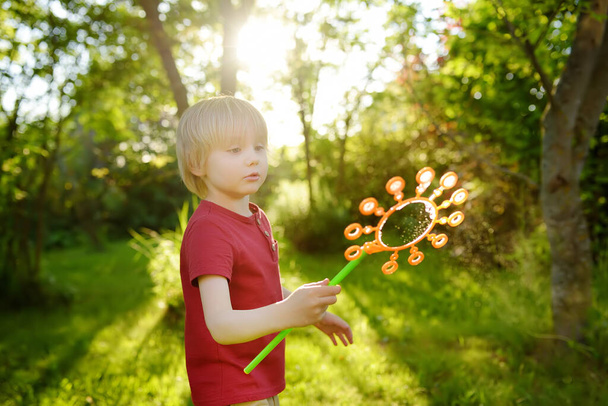 Cute little boy is playing with big soap bubbles outdoor. Child is blowing big and small bubbles simultaneously. Active summer leisure for kids. - Foto, imagen
