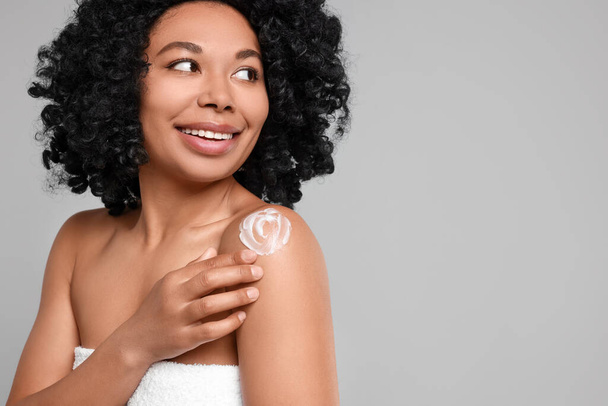 Young woman applying body cream onto shoulder on grey background. Space for text - Foto, Imagen
