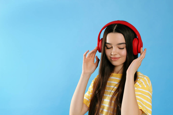 Teenage girl listening music with headphones on light blue background. Space for text - Foto, Imagem