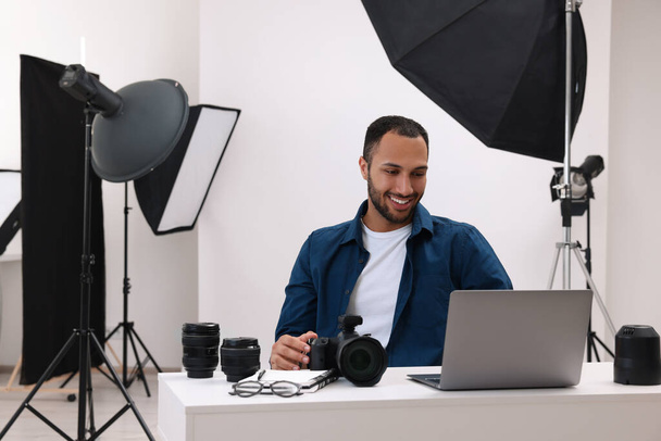 Young professional photographer with camera working on laptop in modern photo studio, space for text - Фото, изображение