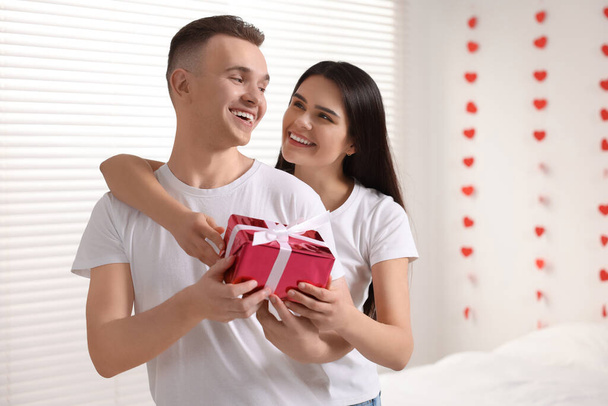 Girlfriend presenting gift to her boyfriend indoors, space for text. Valentine`s day celebration - Photo, Image