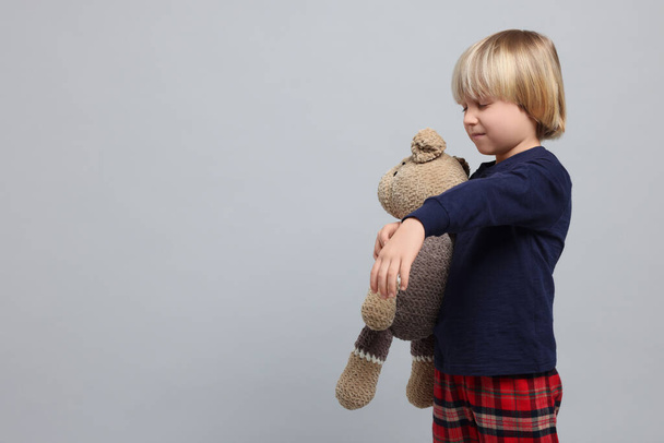 Boy in pajamas with toy bear sleepwalking on light gray background, space for text - Foto, afbeelding