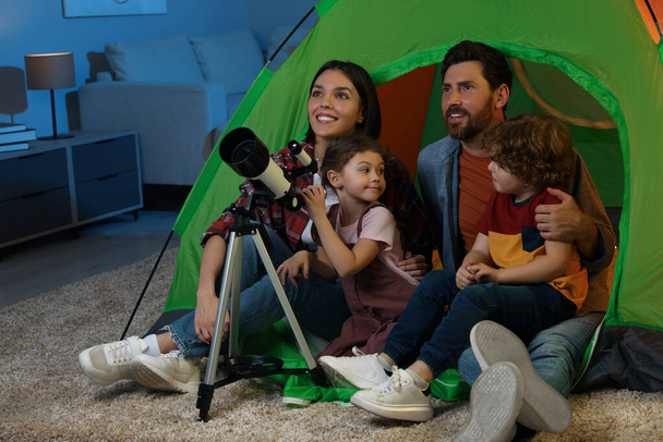Happy family using telescope to look at stars while sitting in camping tent indoors - Foto, imagen