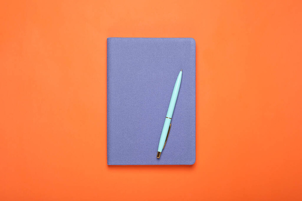 Closed blue notebook and pen on orange background, top view - Photo, image
