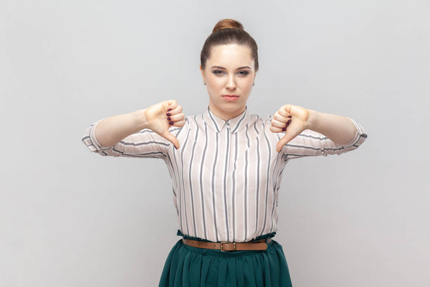 Portrait of dissatisfied displeased attractive woman wearing striped shirt and green skirt standing showing dislike gesture, looks unhappy. Indoor studio shot isolated on gray background. - Фото, изображение