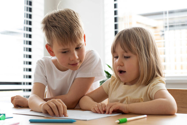 The older brother teaches the younger sister to read letters. The concept of brother and sister, home schooling. - Valokuva, kuva