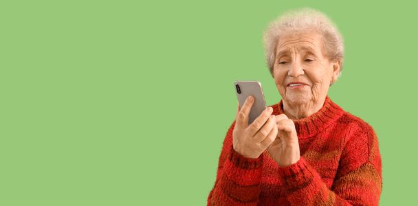 Seniorin benutzt Handy auf grünem Hintergrund mit Platz für Text - Foto, Bild