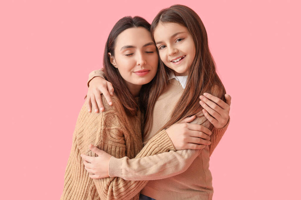 Κοριτσάκι και η μητέρα της με πλεκτά πουλόβερ αγκαλιασμένοι σε ροζ φόντο - Φωτογραφία, εικόνα