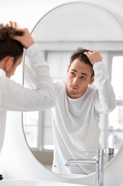 Молодий чоловік з проблемою випадіння волосся дивиться в дзеркало вдома - Фото, зображення