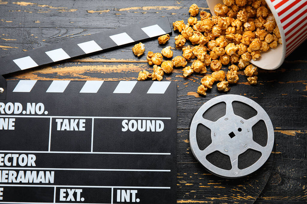 Secchio con gustosi popcorn, clapperboard e bobina di film su sfondo di legno nero - Foto, immagini