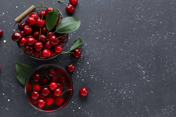 Basket and glass bowl with sweet cherries on black background - Fotoğraf, Görsel