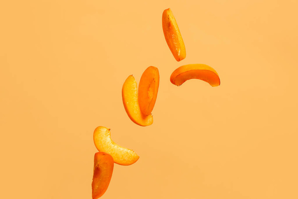 Flying pieces of fresh apricot on orange background - Foto, afbeelding